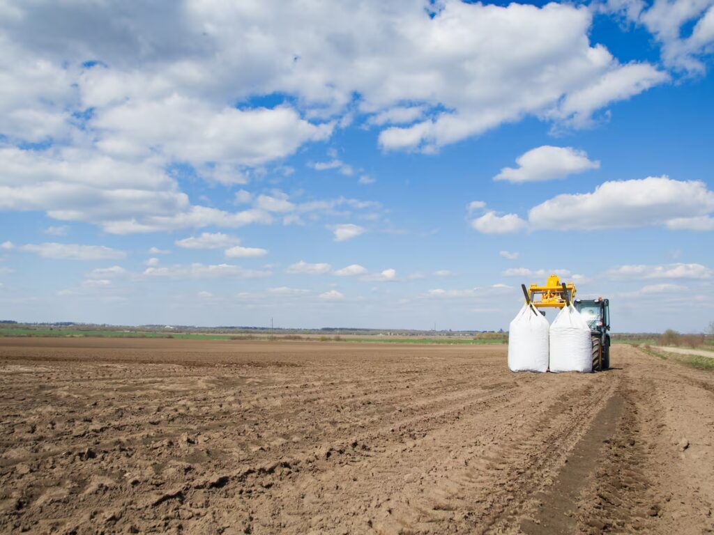 Una maquina dejando dos sacos de abono en un campo de tierra